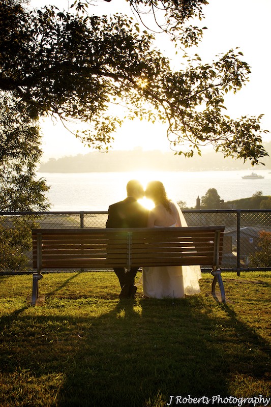 Couple sitting on bench kissing with setting sun behind - wedding photography sydney